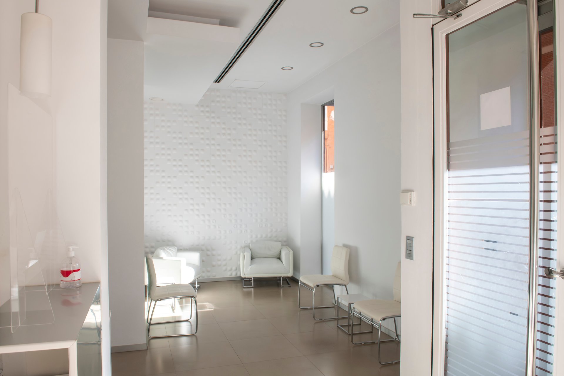 Spotless white waiting area in a contemporary dental clinic, featuring comfortable chairs and a calming ambiance with textured walls and frosted glass doors