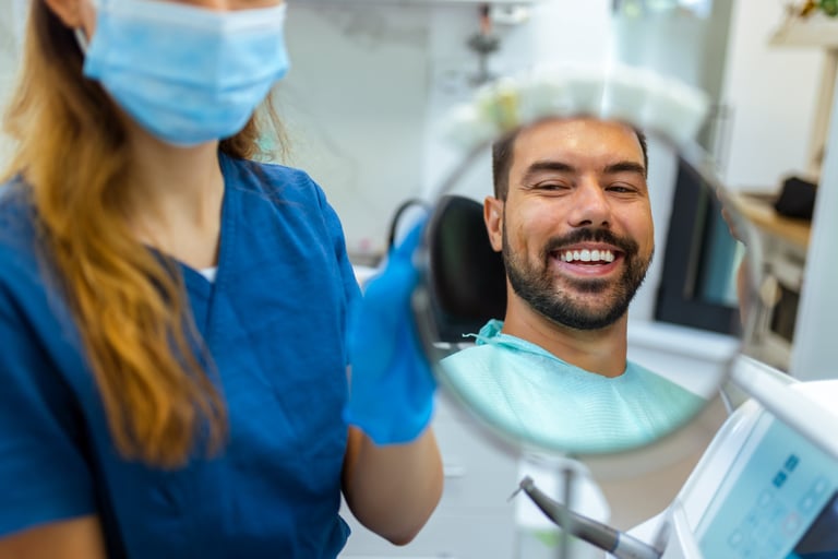 Female dentist helping male patient see his smile using a small mirror during dental checkup in modern clinic