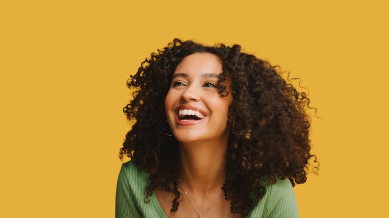 Close up studio portrait of young laughing woman with radiant healthy smile standing against yellow background