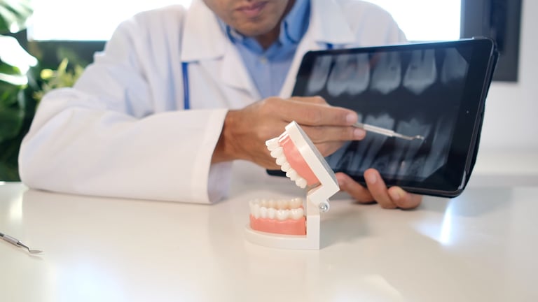Dentist pointing at digital dental x-ray on tablet while illustrating oral health concepts with jaw model to patient