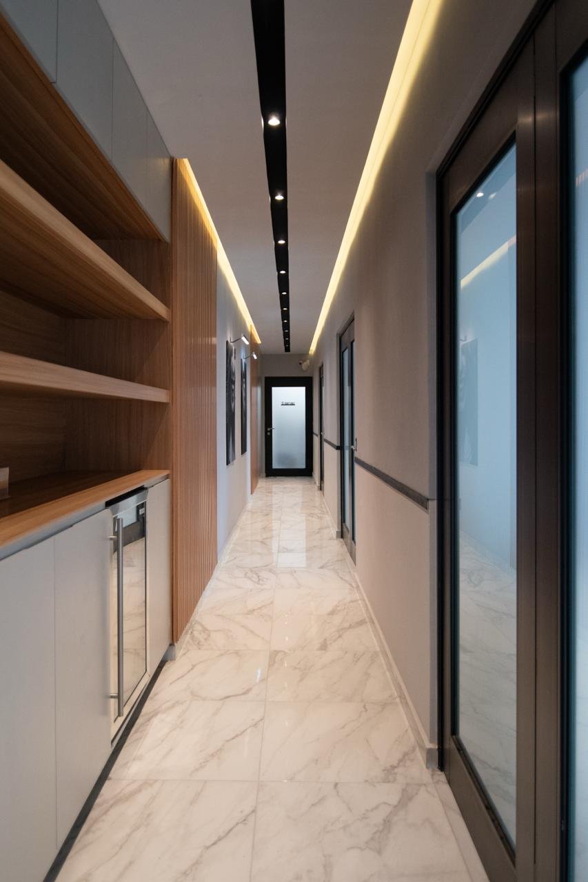 Pasillo moderno con piso de mármol, estantes de madera en pared y luces empotradas en techo