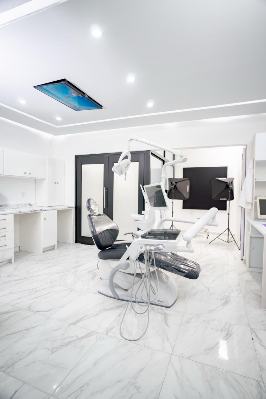 Consultorio dental moderno con piso de mármol blanco, silla dental y pantalla en el techo