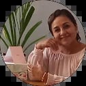 Woman in peach top holding green potted plant, smiling at camera indoors