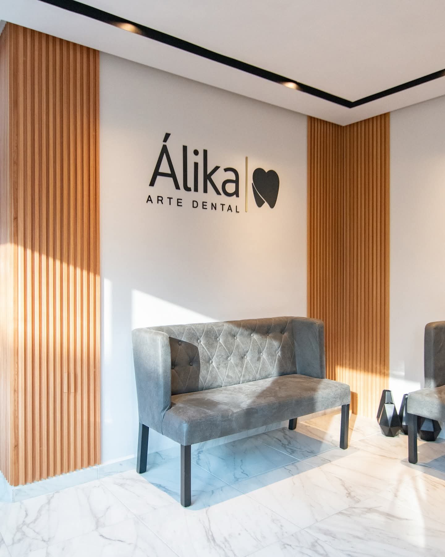 Modern dental office waiting area with Alika Arte Dental signage, blue upholstered chair, wooden wall panels, and marble flooring