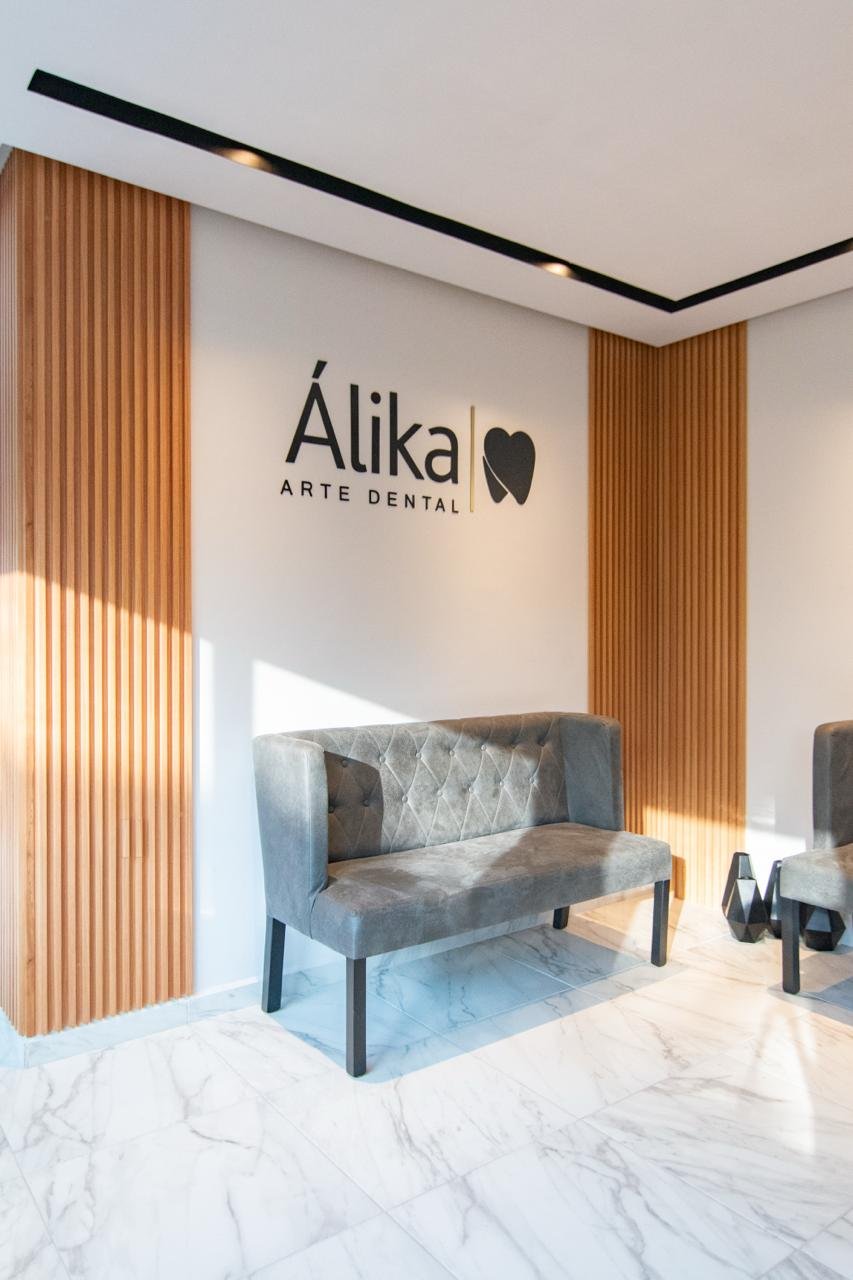 Área de recepción moderna de Alika Arte Dental con logo, asientos tapizados y paneles de madera