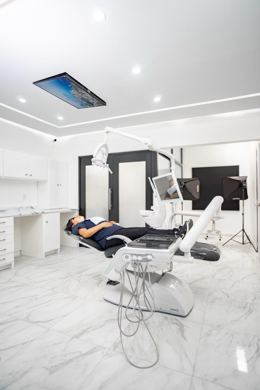 Modern dental office with patient in chair, white marble floors, ceiling-mounted monitor, equipment and sterilization unit